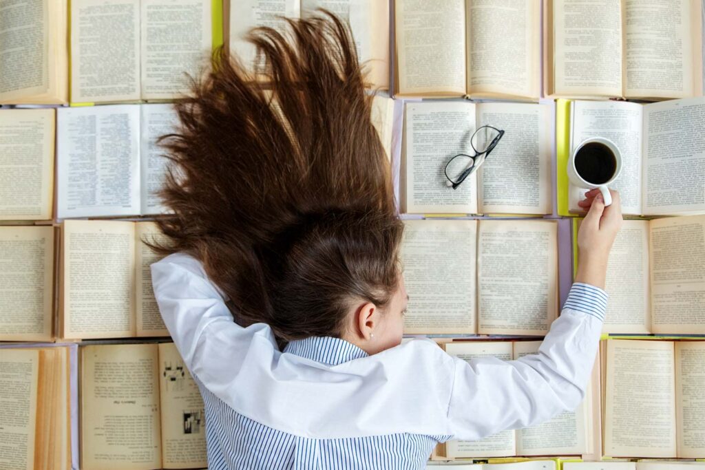 Girl resting on a pile of books with a cup of coffee in her hand